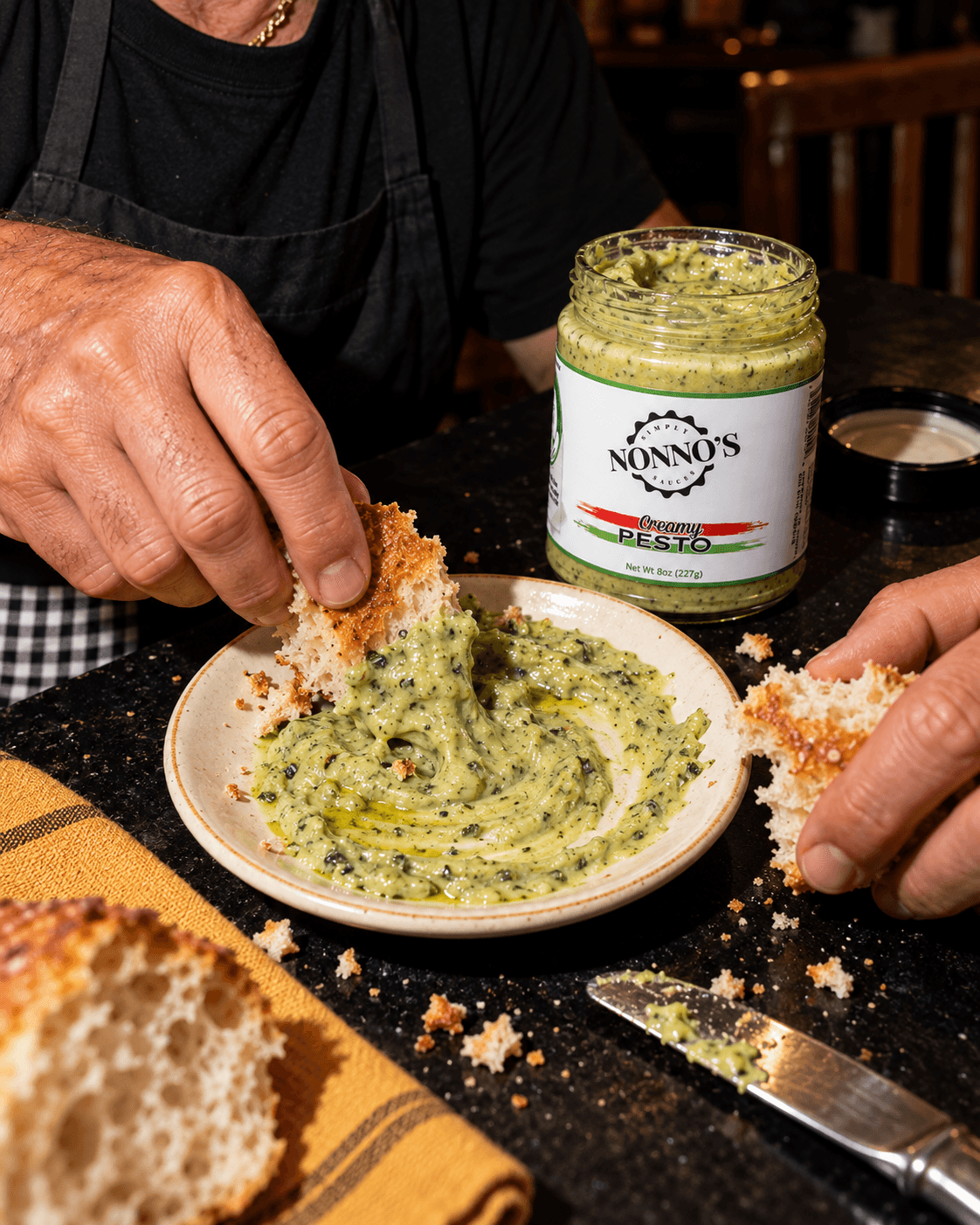 Torn bread dipped into creamy pesto with a jar on the counter.