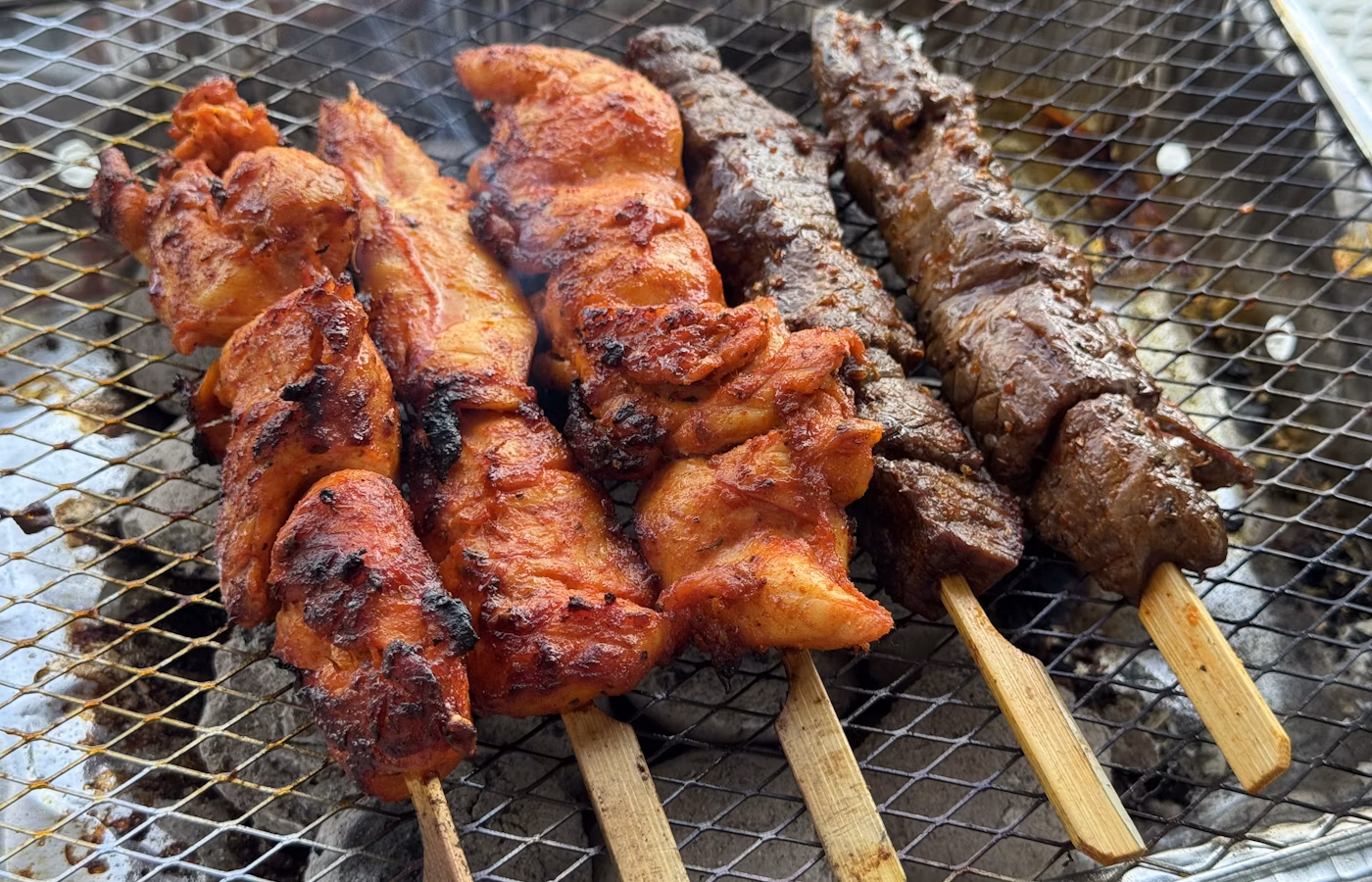 Chicken skewers grilling over coals